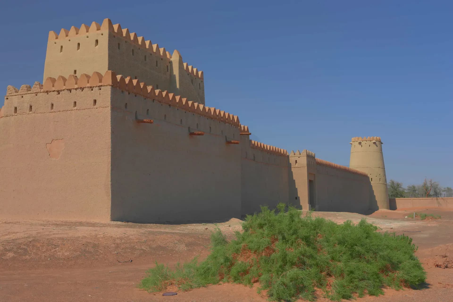 Mezyad Fort in Al Ain, a restored mud-brick fort rising above the desert under a clear blue sky.
